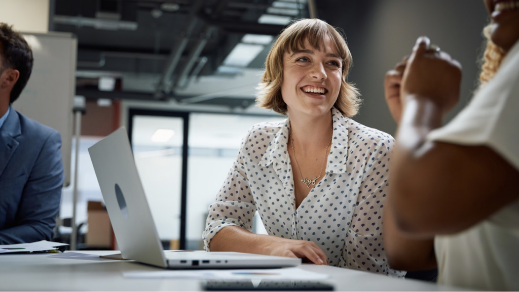 A women sitting at a table with her computer smiling and talking